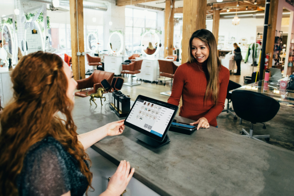Set in a salon environment, an employee is behind the desk processing payment from a customer.