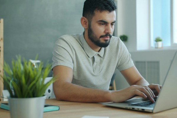 A man sitting at a desk typing on a laptop computer